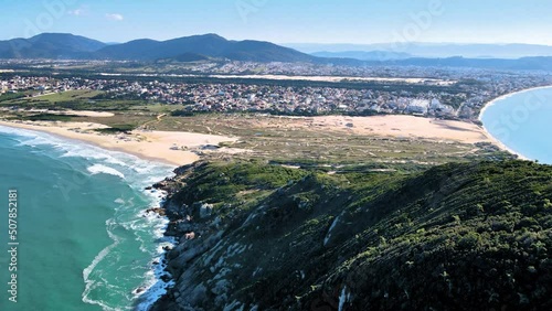 Aerial drone scene of urbanized paradise beach with sand dunes, mountains and sea beach of santinho Florianópolis mountain top and city on the horizon photo
