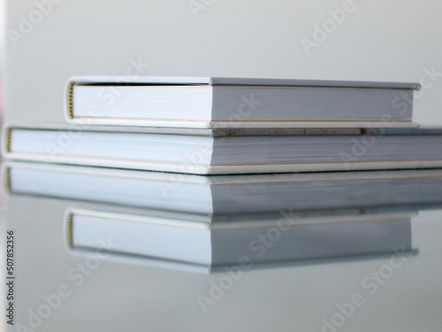 Macro photo of two closed photobooks in white and beige, lie on a glossy textured blue tabletop.