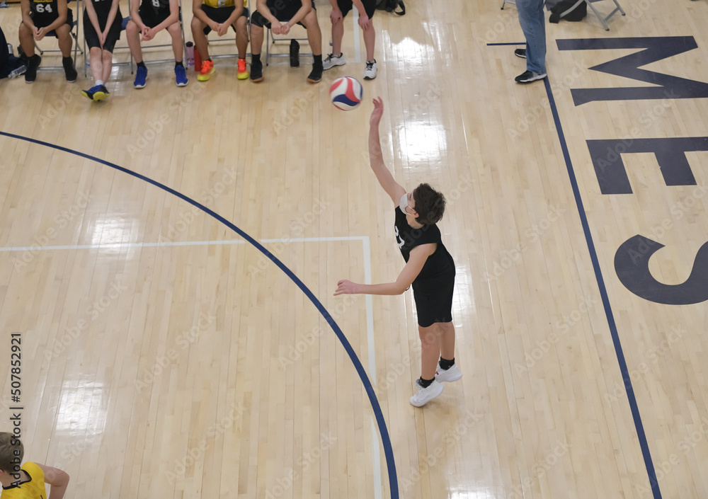 Volleyball player serving the ball while bench players watch Stock