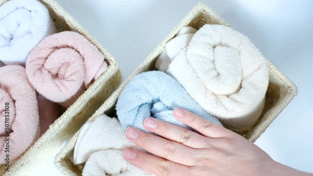 Female hand folds rolled towels in a wicker box close-up top view on white background. Female hand folds rolled towels in a wicker box close-up top view on white background.