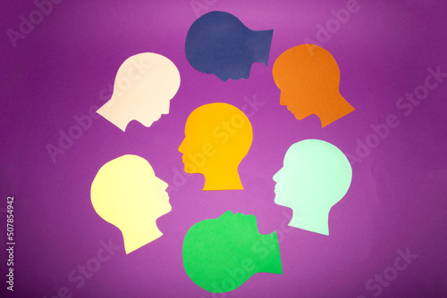 central orange paper head around her colorful heads facing her, creative concept, lead role, most important factor, indispensable factor, purple background