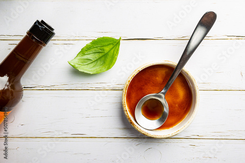 Worcestershire sauce in a bowl with spoon and bottle over white background, top view photo