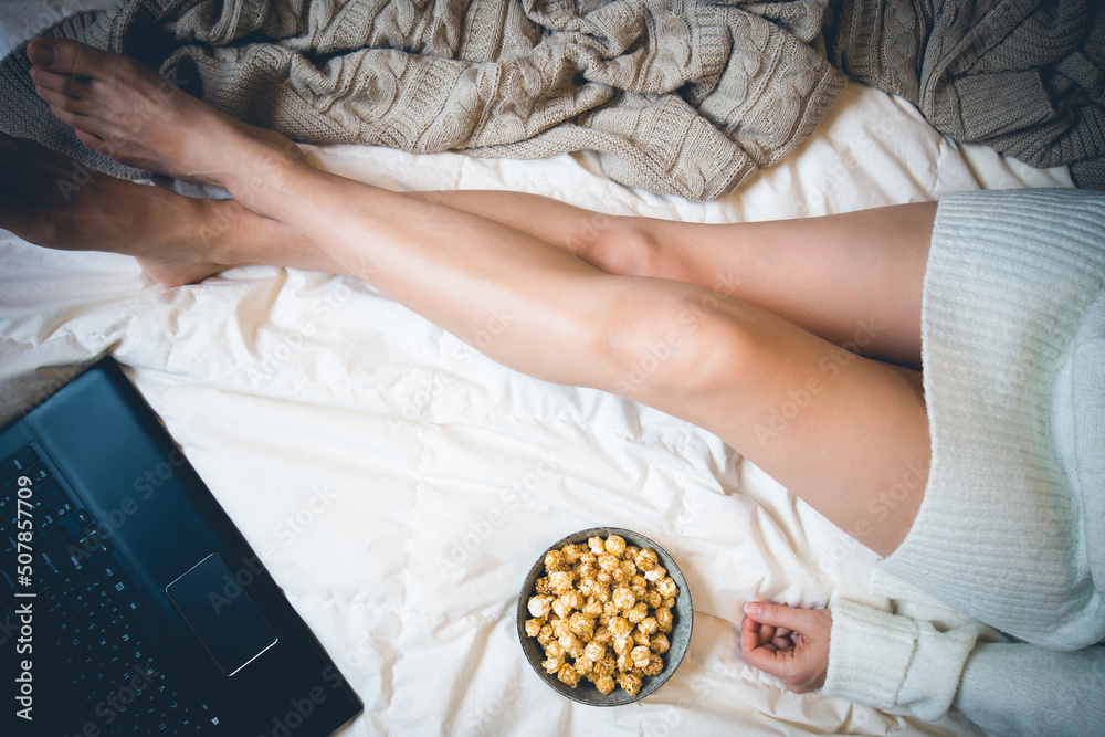 Obraz premium Young woman eating pop corn at home in her bed and checking her laptop or watching movie, top view, flat lay