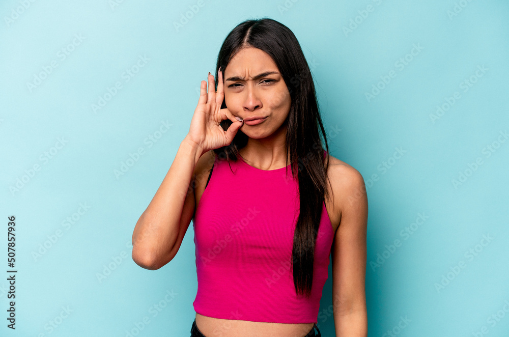 Fototapeta premium Young hispanic woman isolated on blue background with fingers on lips keeping a secret.