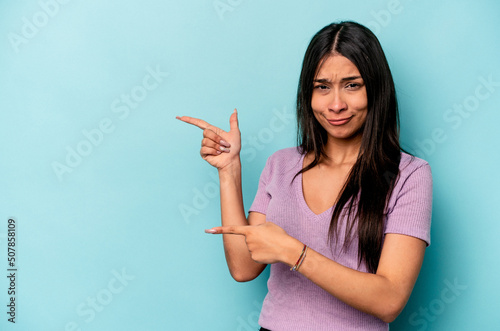 Young hispanic woman isolated on blue background shocked pointing with index fingers to a copy space.