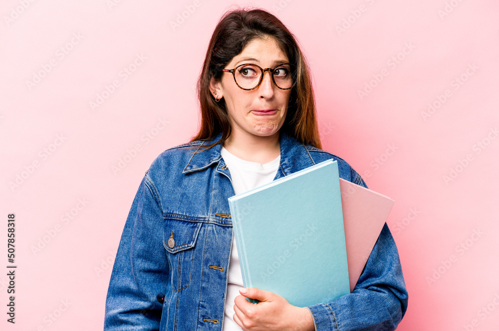 Fototapeta premium Young student caucasian woman isolated on pink background confused, feels doubtful and unsure.