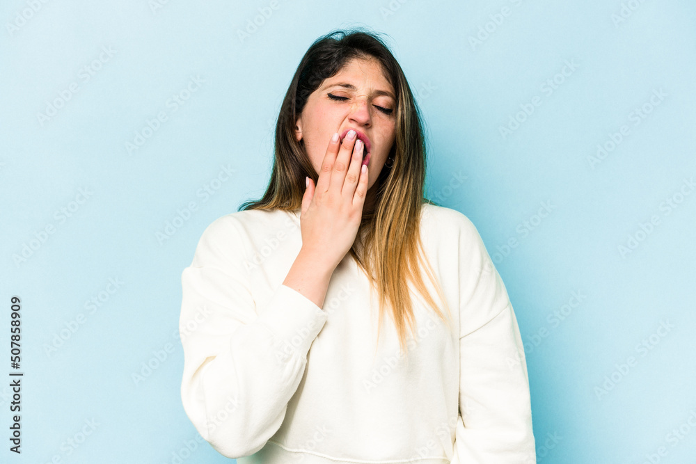 Young caucasian woman isolated on blue background yawning showing a tired gesture covering mouth with hand. Young caucasian woman isolated on blue background yawning showing a tired gesture covering mouth with hand.