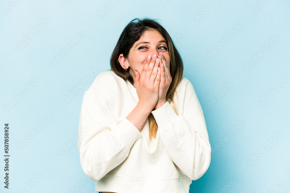 Young caucasian woman isolated on blue background laughing about something, covering mouth with hands. Young caucasian woman isolated on blue background laughing about something, covering mouth with hands.