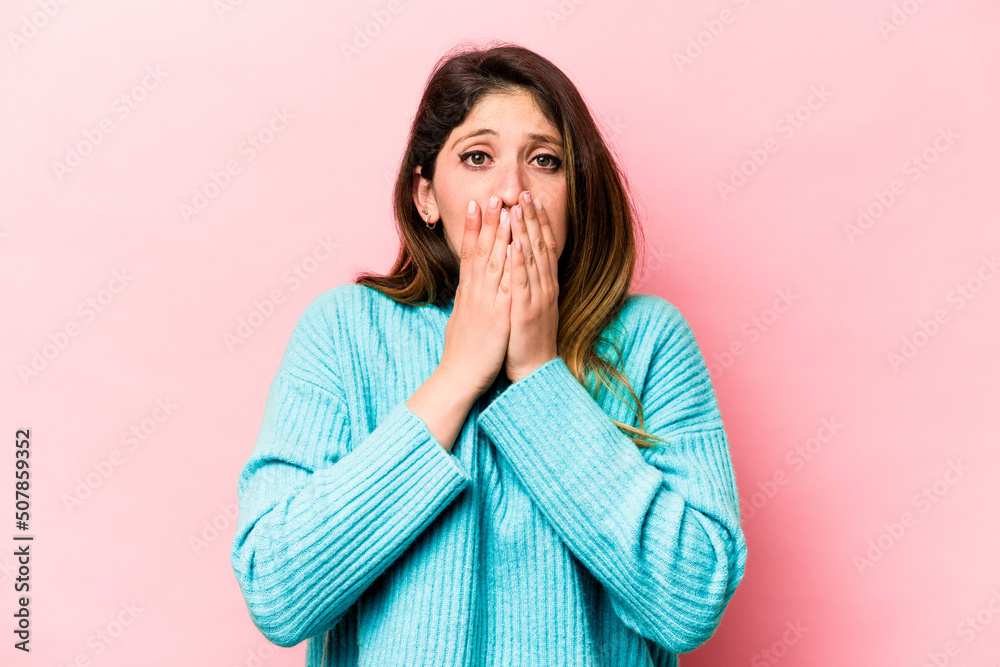 Young caucasian woman isolated on pink background covering mouth with hands looking worried.