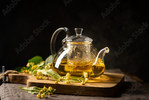 teapot of herbal tea with linden flowers on dark background
