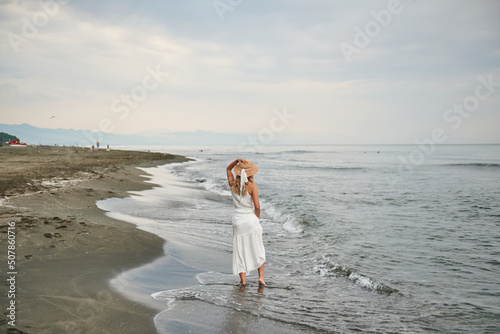 a girl in a hat and a white dress walks on the beach