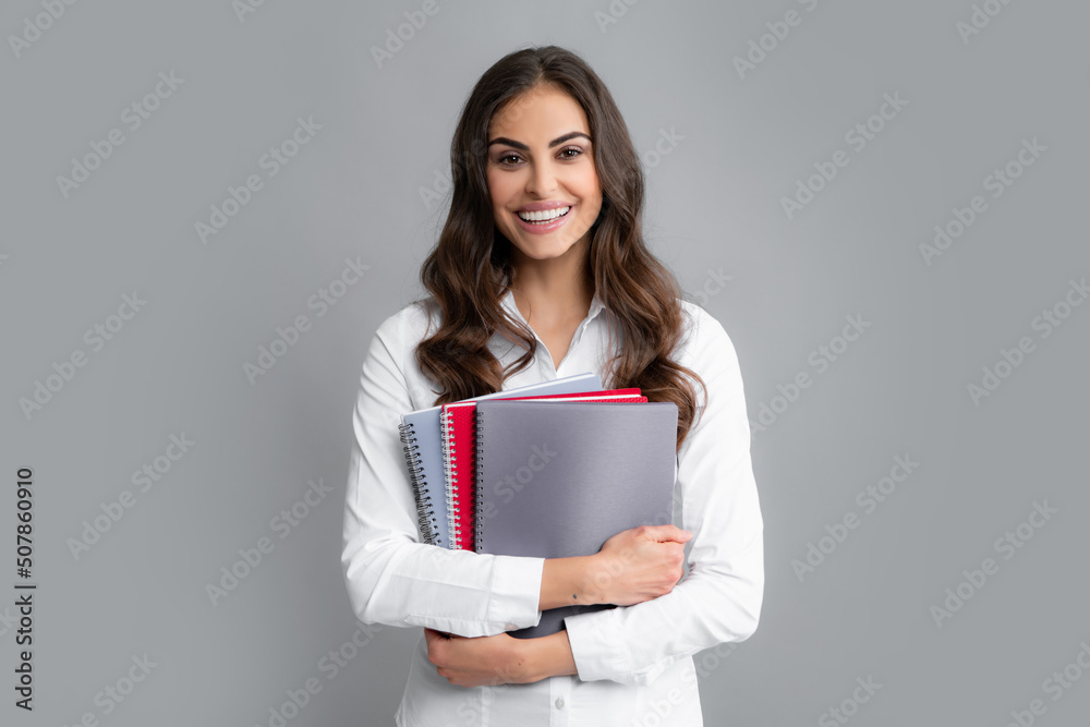 Portrait of happy smiling student or teacher. College or high school ducation. Young woman with notebooks smiling at camera on gray studio background. Young female university student. Portrait of happy smiling student or teacher. College or high school ducation. Young woman with notebooks smiling at camera on gray studio background. Young female university student.