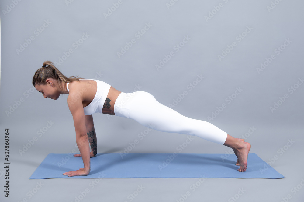 Full length fitness woman in white sportswear sitting on gym mat and practicing yoga, isolated on gray background.