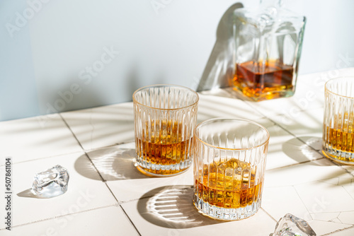 Whiskey with ice in glasses and bottle, white background with hard light, shadow Fototapet