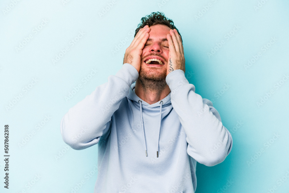 Young caucasian man isolated on blue background laughs joyfully keeping hands on head. Happiness concept. Young caucasian man isolated on blue background laughs joyfully keeping hands on head. Happiness concept.