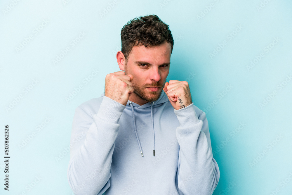 Young caucasian man isolated on blue background throwing a punch, anger, fighting due to an argument, boxing. Young caucasian man isolated on blue background throwing a punch, anger, fighting due to an argument, boxing.