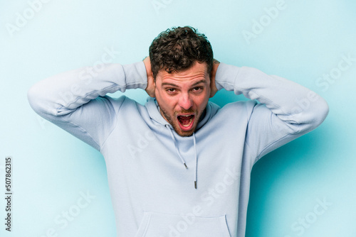 Young caucasian man isolated on blue background screaming, very excited, passionate, satisfied with something.