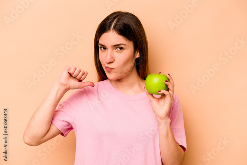 Young hispanic woman holding an apple isolated on beige background feels proud and self confident, example to follow. © Asier