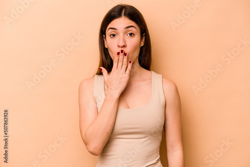 Young hispanic woman isolated on beige background shocked, covering mouth with hands, anxious to discover something new.