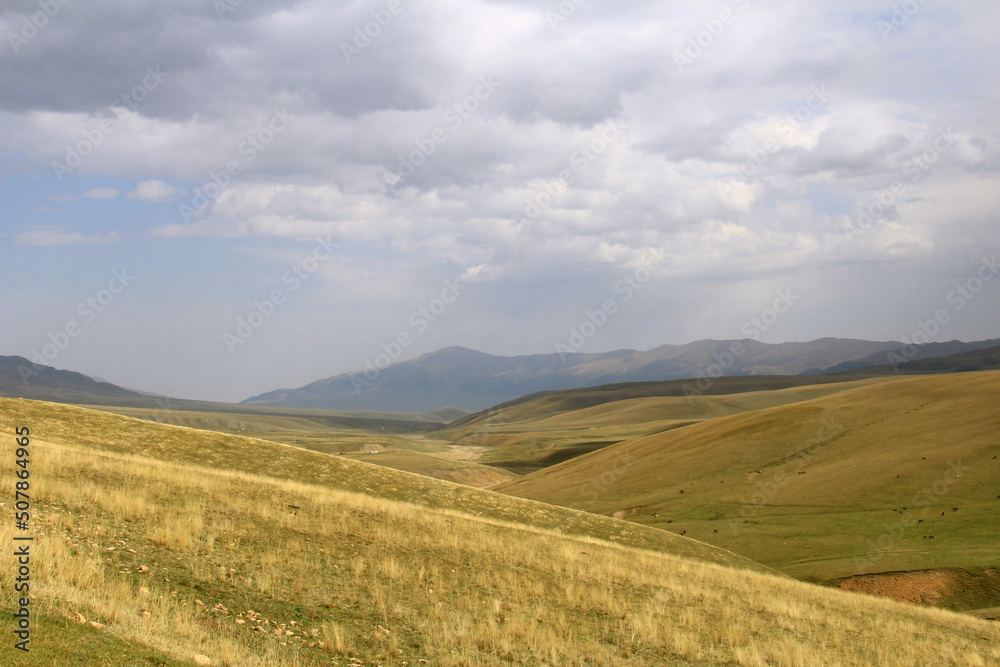 Fototapeta premium Steppe and hilly landscape with a view of the mountain ranges on the Assy plateau in autumn against the background of the sky with clouds, panorama