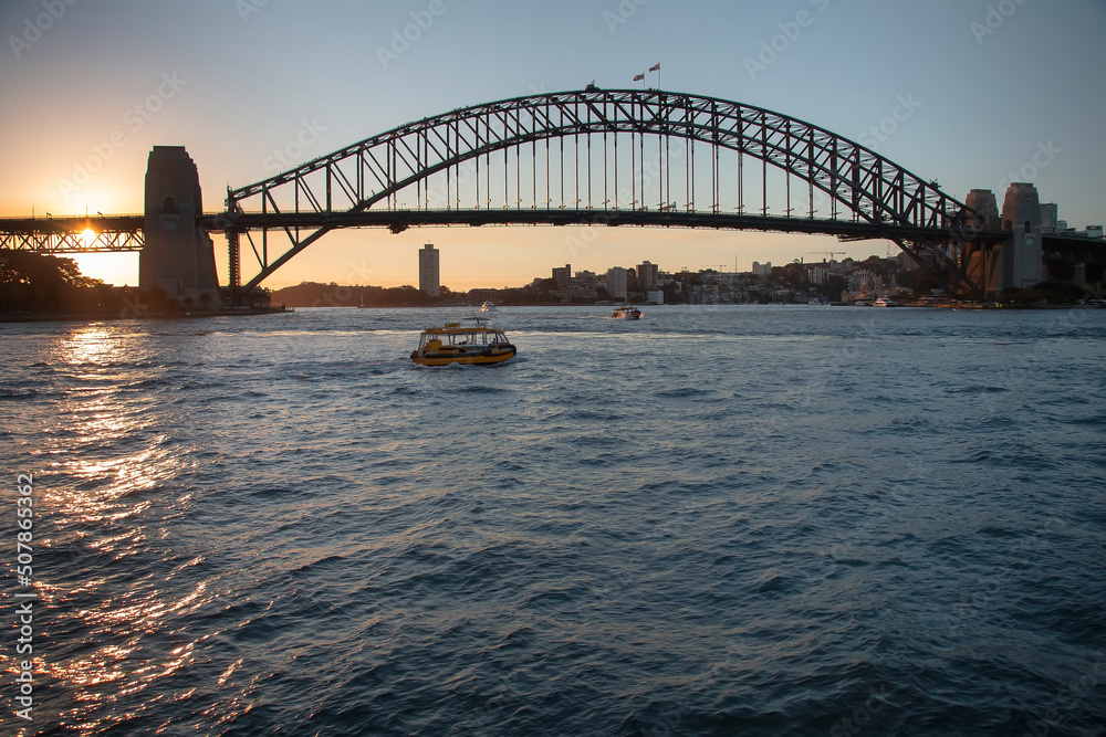 Naklejka premium Large bridge across the bay at sunset with a small boat on the water, Harbour Bridge, Sydney, Australia