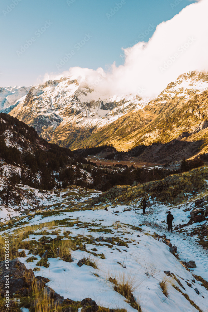 Hikers in mountain path, autum and winter view in pyrenees with snowed mountains in background