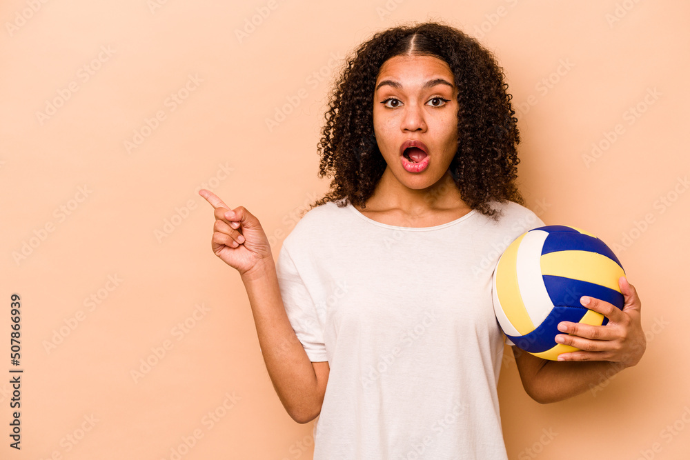 Young African American woman playing volleyball isolated on beige background pointing to the side