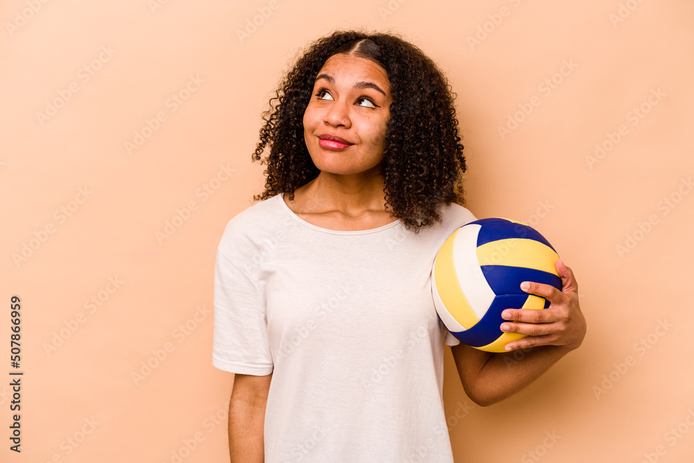 Young African American woman playing volleyball isolated on beige background dreaming of achieving goals and purposes