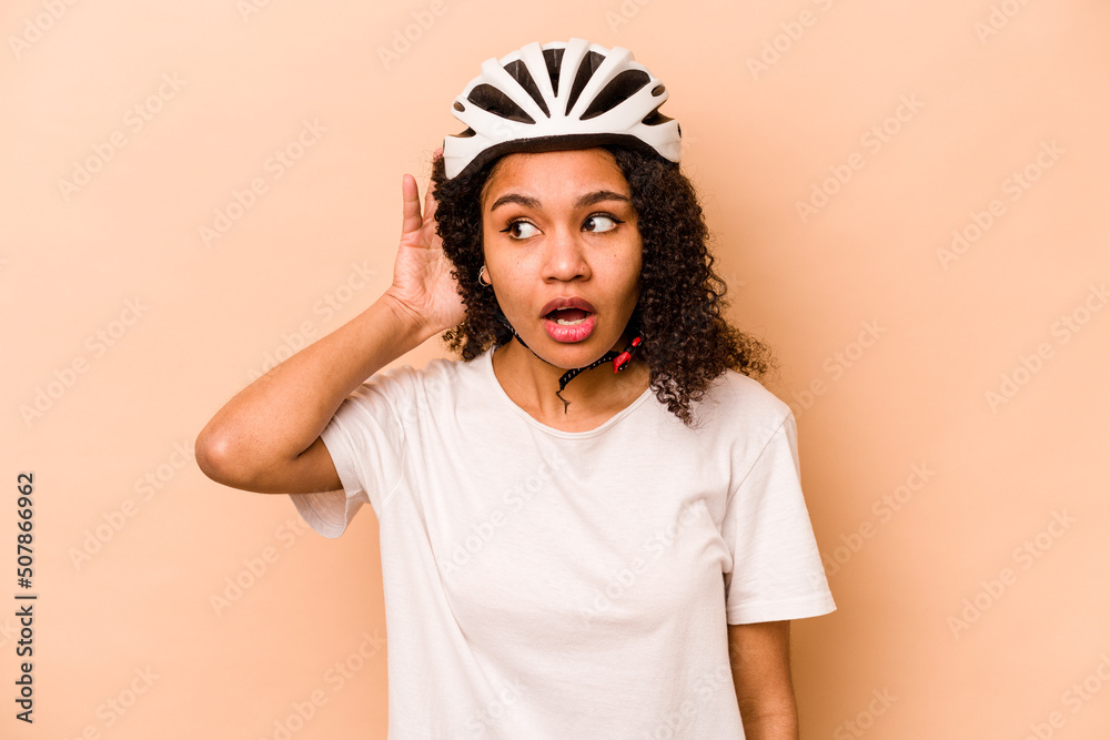 Young hispanic woman wearing a helmet bike isolated on blue background trying to listening a gossip. Young hispanic woman wearing a helmet bike isolated on blue background trying to listening a gossip.