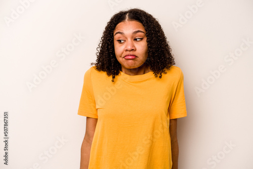 Young African American woman isolated on white background shrugs shoulders and open eyes confused. © Asier