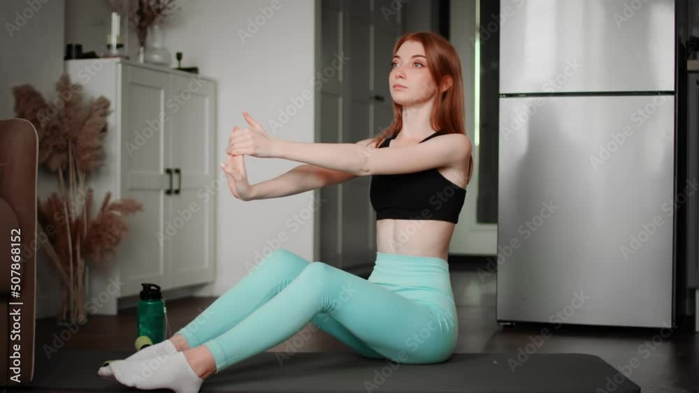 The girl is warming up while sitting on a rug in the living room in sportswear. Sport The girl is warming up while sitting on a rug in the living room in sportswear. Sport