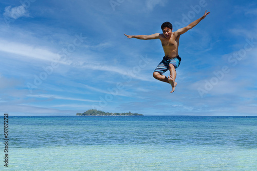 Young man jumping in the air at the beach of Raja Ampat. Carefree people vacation time concept image.