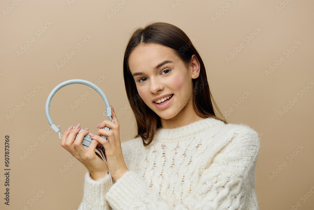 a beautiful, happy woman in a white sweater stands on a gray studio background holding large headphones in her hands a beautiful, happy woman in a white sweater stands on a gray studio background holding large headphones in her hands