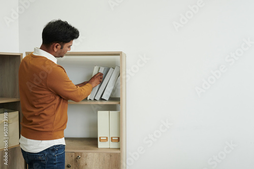 Businessman taking binder from shelf in office, view from the back