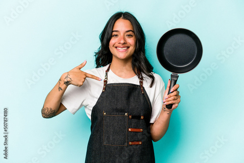 Vászonkép Young hispanic cooker woman holding frying pan isolated on blue background perso