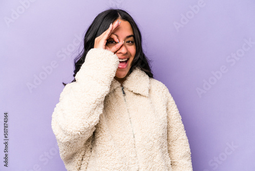 Young hispanic woman isolated on purple background excited keeping ok gesture on eye.