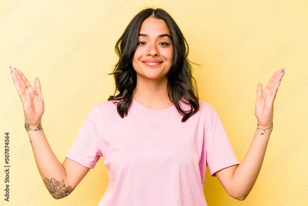 Young hispanic woman isolated on yellow background holding something little with forefingers, smiling and confident. Young hispanic woman isolated on yellow background holding something little with forefingers, smiling and confident.