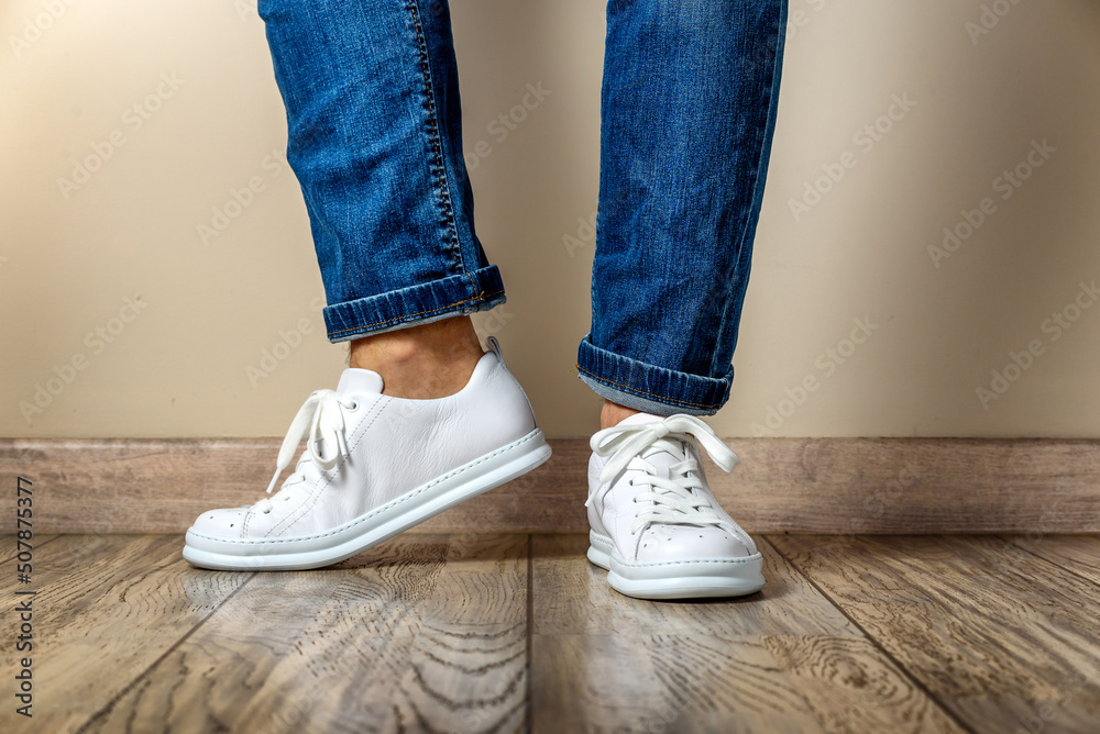 Man in Stylis New White Sneakers and jeans standing at parquet floor at home
