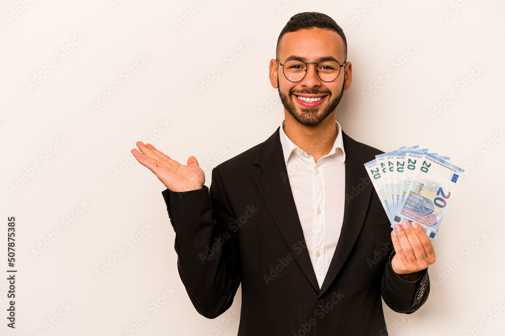 Young business hispanic man holding banknotes isolated on white background showing a copy space on a palm and holding another hand on waist. Young business hispanic man holding banknotes isolated on white background showing a copy space on a palm and holding another hand on waist.