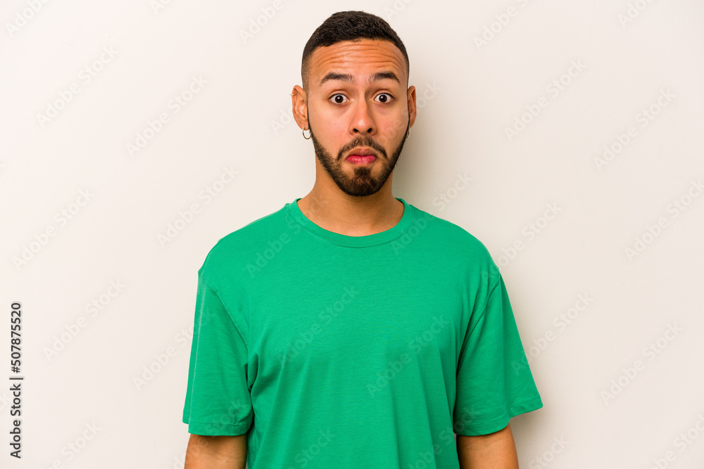 Obraz premium Young hispanic man isolated on white background shrugs shoulders and open eyes confused.