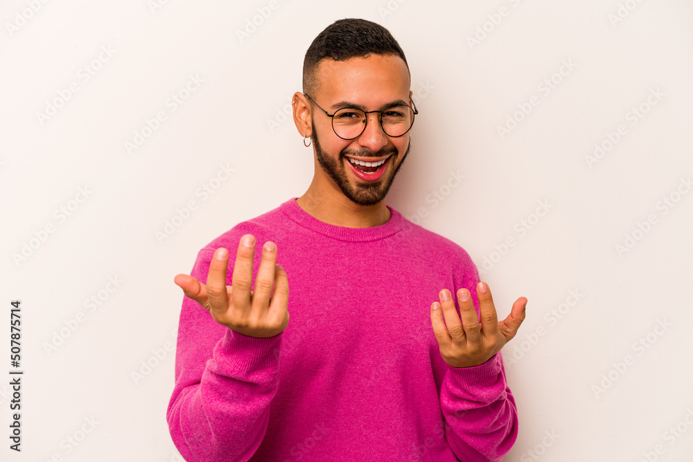 Naklejka premium Young hispanic man isolated on white background pointing with finger at you as if inviting come closer.
