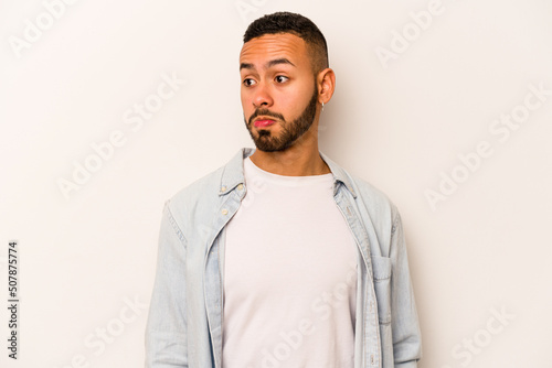 Young hispanic man isolated on white background shrugs shoulders and open eyes confused.