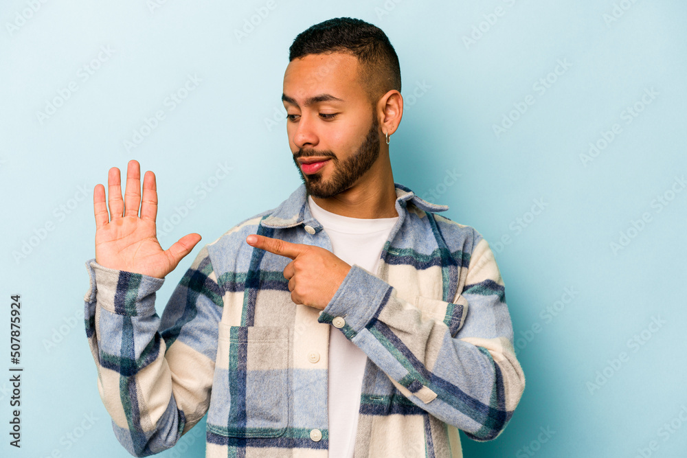 Young hispanic man isolated on blue background smiling cheerful showing number five with fingers.