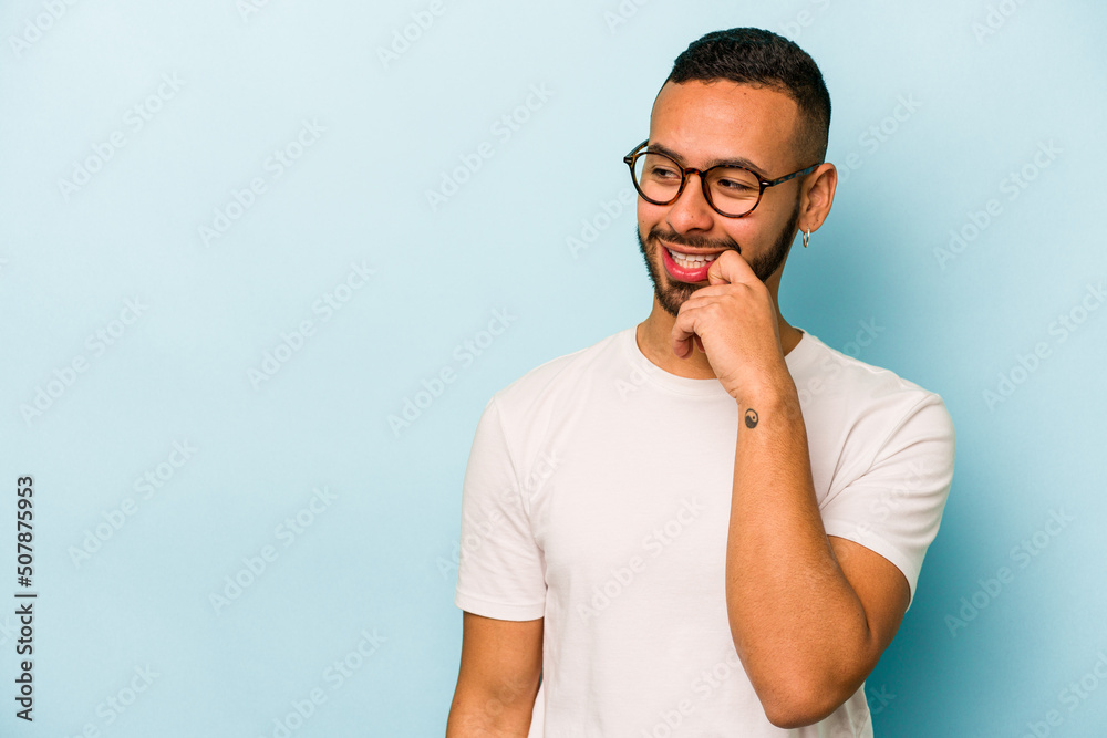Young hispanic man isolated on blue background relaxed thinking about something looking at a copy space. Young hispanic man isolated on blue background relaxed thinking about something looking at a copy space.