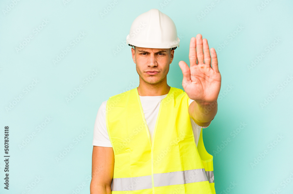 Young laborer caucasian man isolated on blue background standing with outstretched hand showing stop sign, preventing you.