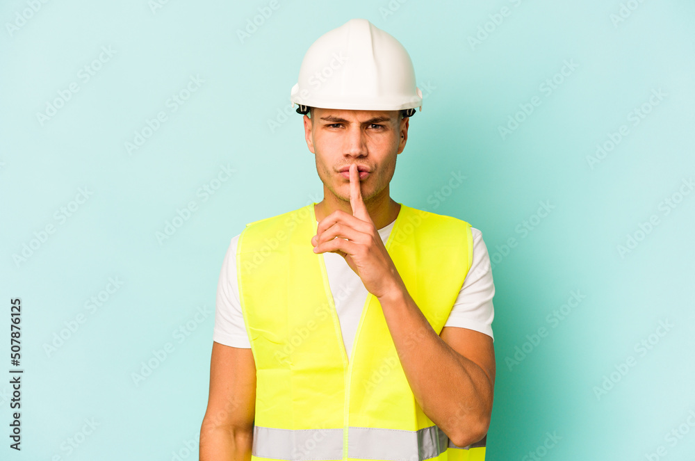 Young laborer caucasian man isolated on blue background keeping a secret or asking for silence.