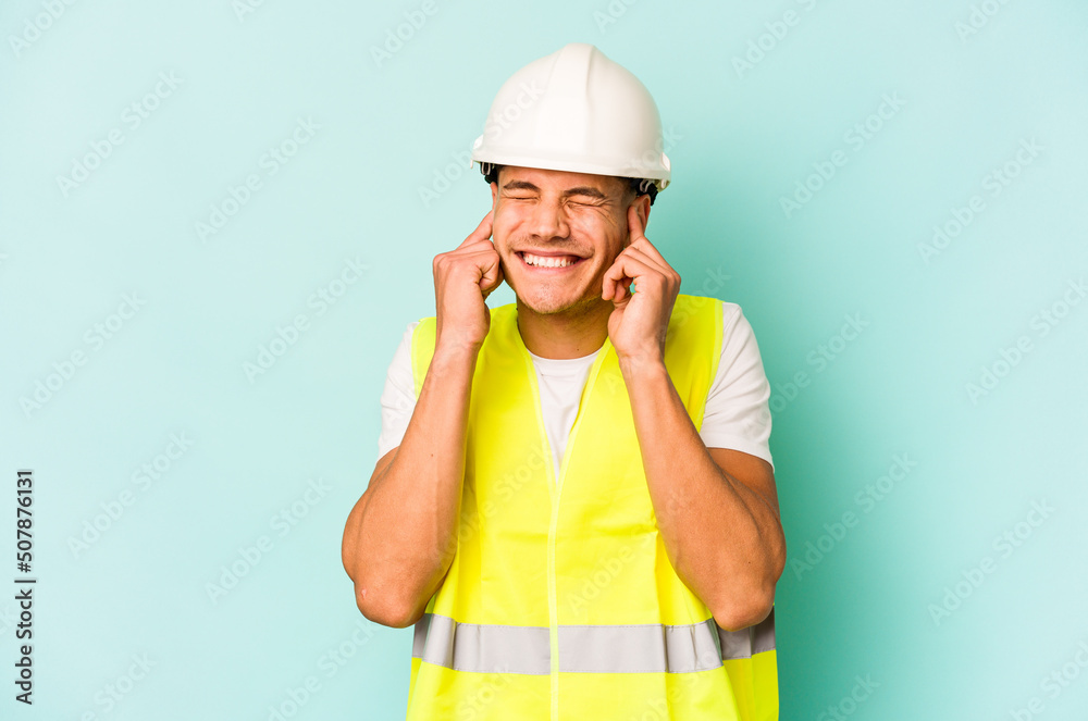 Young laborer caucasian man isolated on blue background covering ears with hands. Young laborer caucasian man isolated on blue background covering ears with hands.