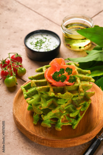 Green Belgian waffles. Spinach or wild garlic or pesto waffles with red salmon and cream sauce on old beige tile table background. Delicious breakfast, snack, brunch on old beige tiles background.