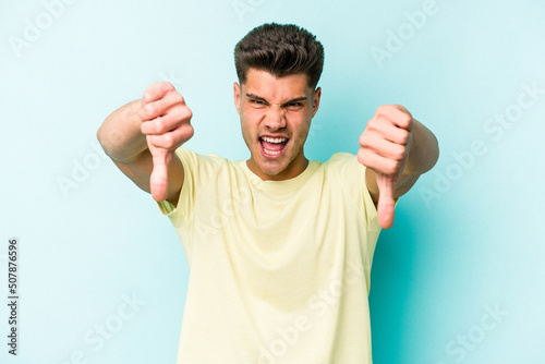 Young caucasian man isolated on blue background showing thumb down and expressing dislike.