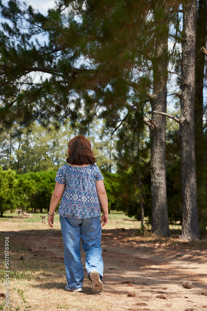Woman seen from the back walking alone along a country road a summer afternoon